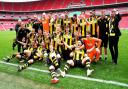 Hebburn Town players and staff celebrate with the FA Vase in front of a vast and empty Wembley Stadium.